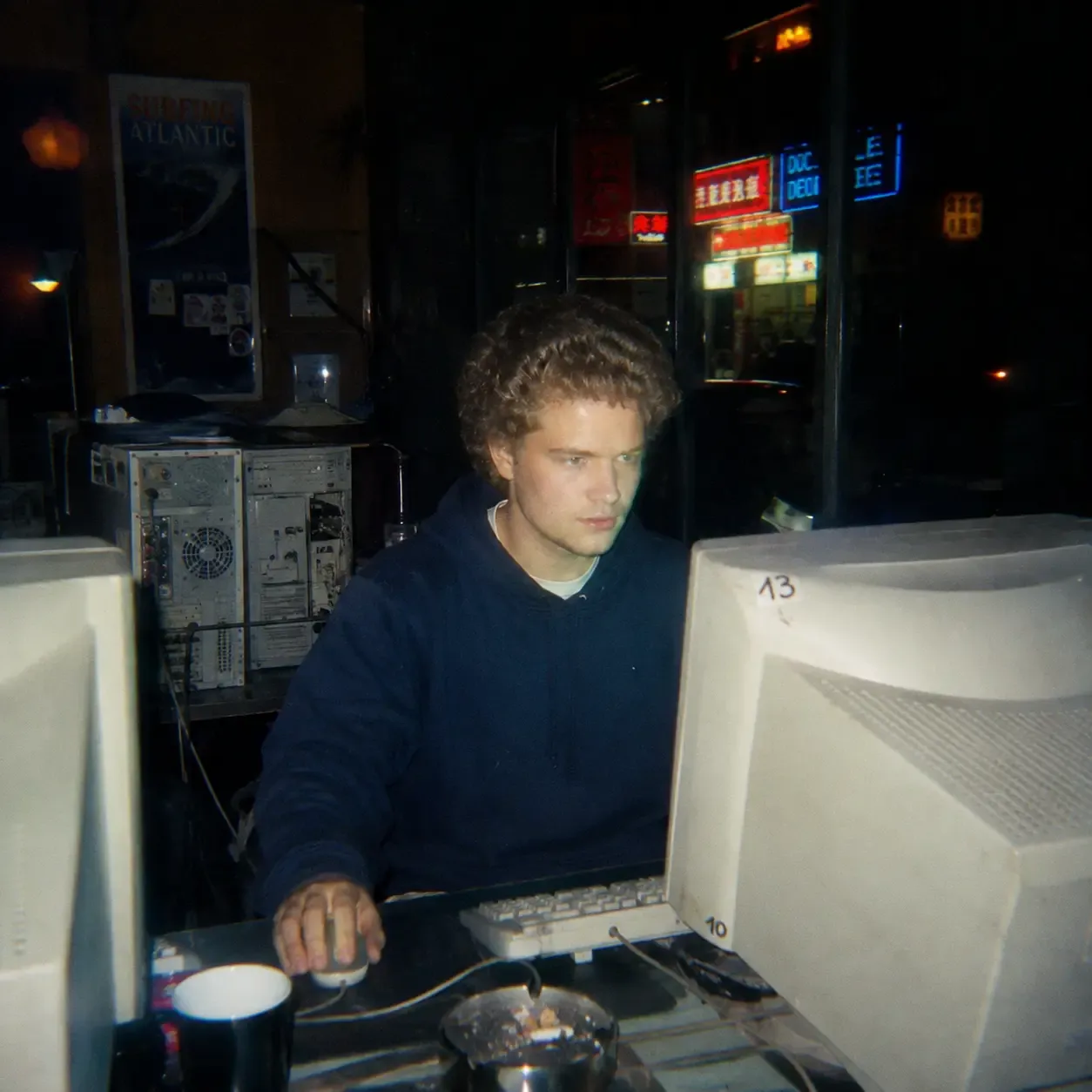 A 1990s internet café at night, lit by a CRT monitor
