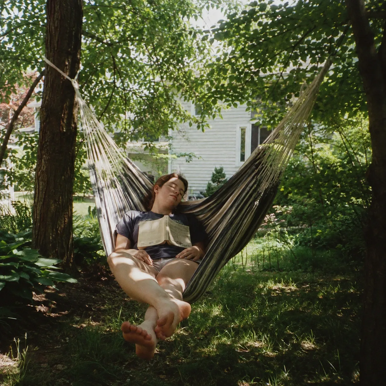 A person resting in a hammock with a book in morning light